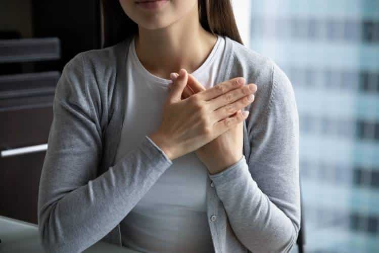 A woman sitting and crossing her hands in front of her heart