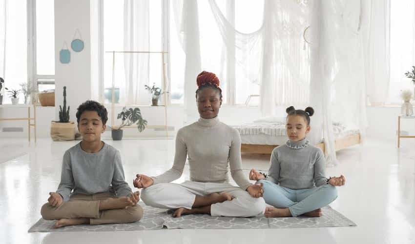 Positive black mother with kids meditating together with closed eyes at home