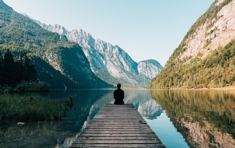 A person peacefully sitting near a lake looking at the mountains